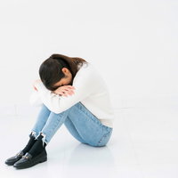 白背景で小山座りして項垂れる悲しい女性の写真