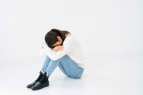 白背景で小山座りして項垂れる悲しい女性