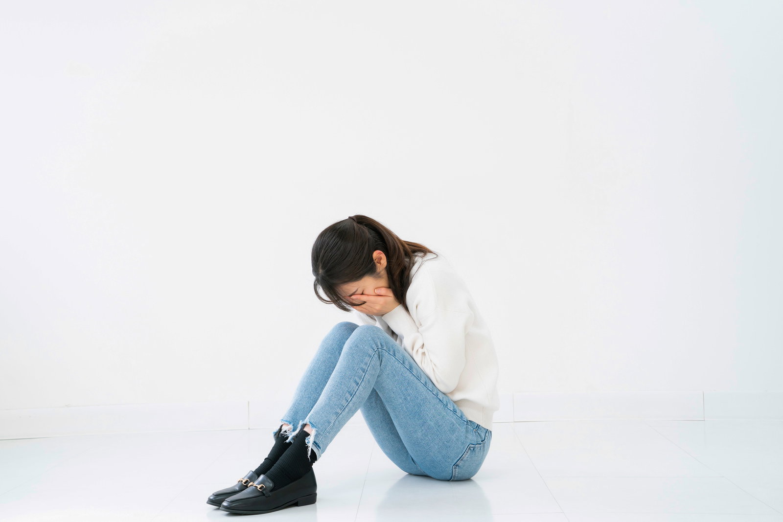 両手で顔を覆いながら蹲る女性［モデル：SAKI］