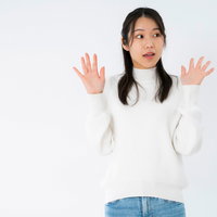 両手を大きく広げて驚く白いニットの女性の写真