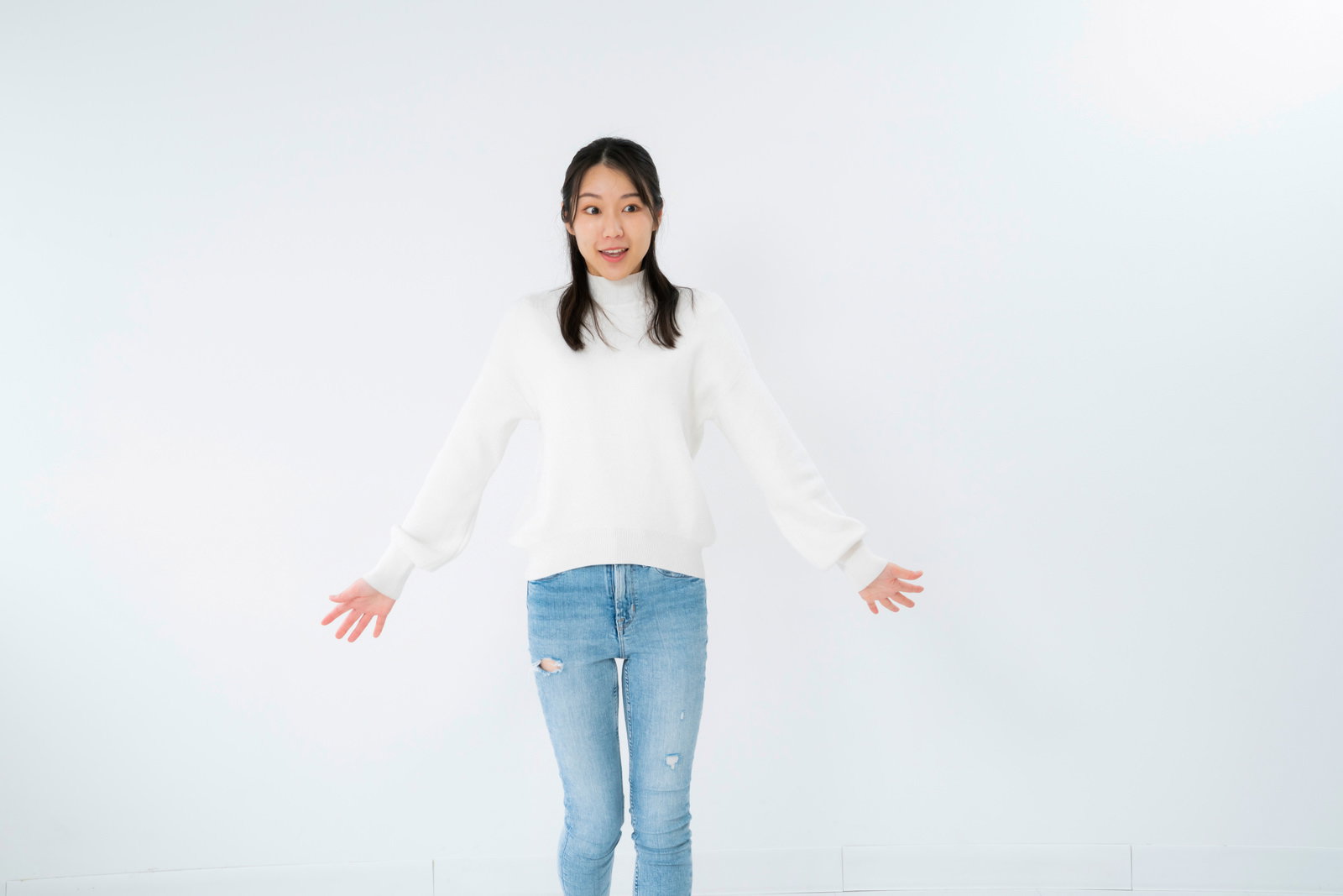 A woman in a white turtleneck with her arms outstretched, showing a surprised expression