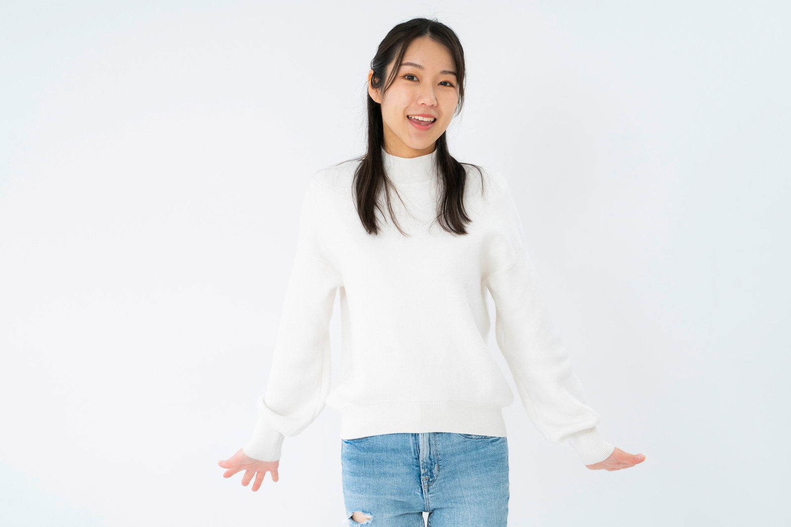 白いニットセーターとジーンズ姿で両手を広げて笑う女性［モデル：SAKI］