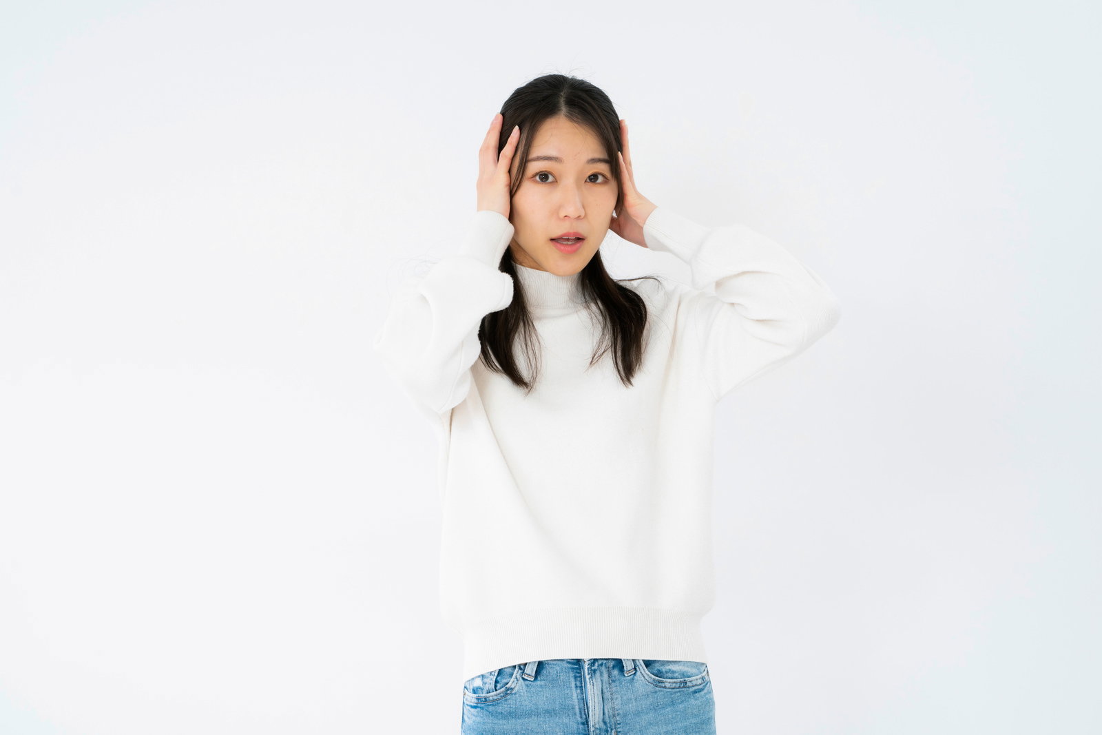 A woman in a white turtleneck sweater holding her head in her hands with a confused expression