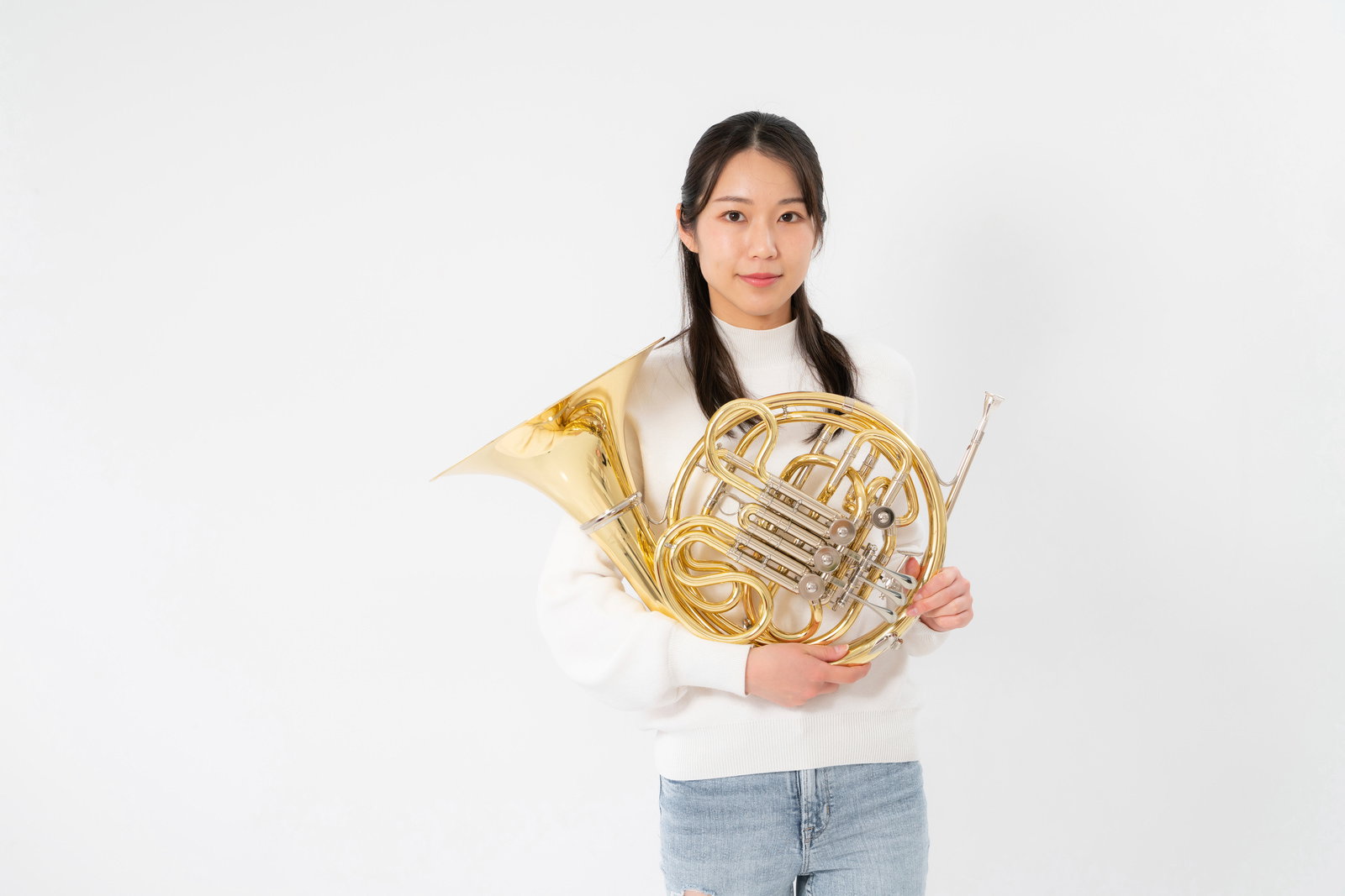 A woman in a white sweater holding a gold-colored horn with both hands