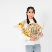 ホルンを両手で持つ白いセーター姿の女性奏者の演奏の写真