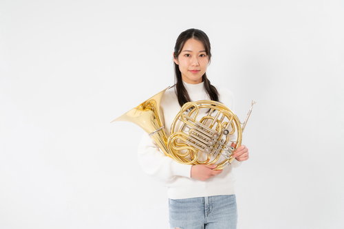 ホルンを両手で持つ白いセーター姿の女性奏者の演奏