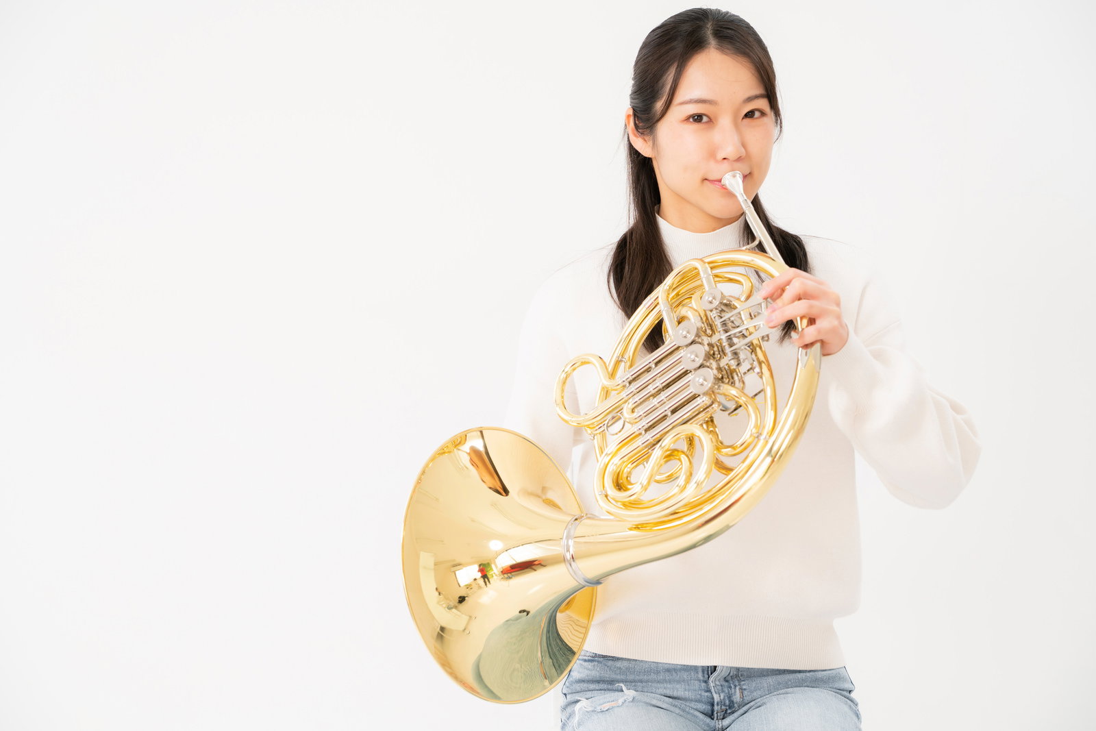 ホルンを吹く女性が楽器を両手で構えて演奏している［モデル：SAKI］