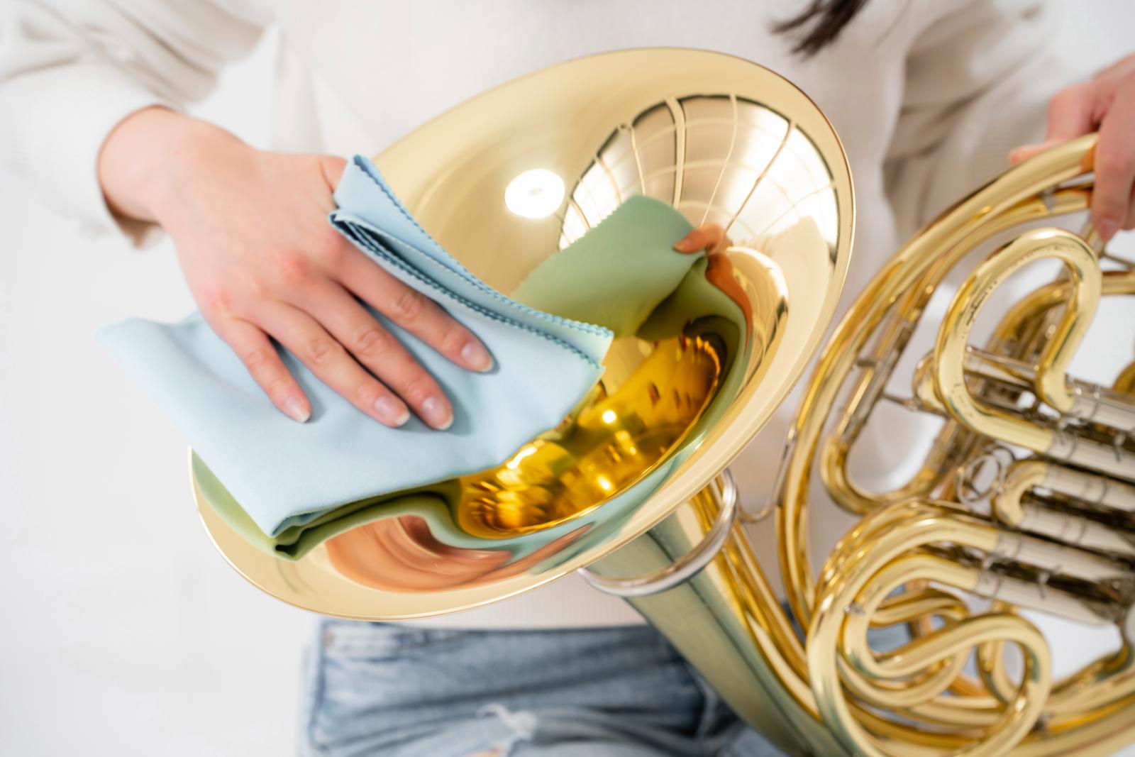 ホルンを布で磨きながらメンテナンスする女性の手元［モデル：SAKI］