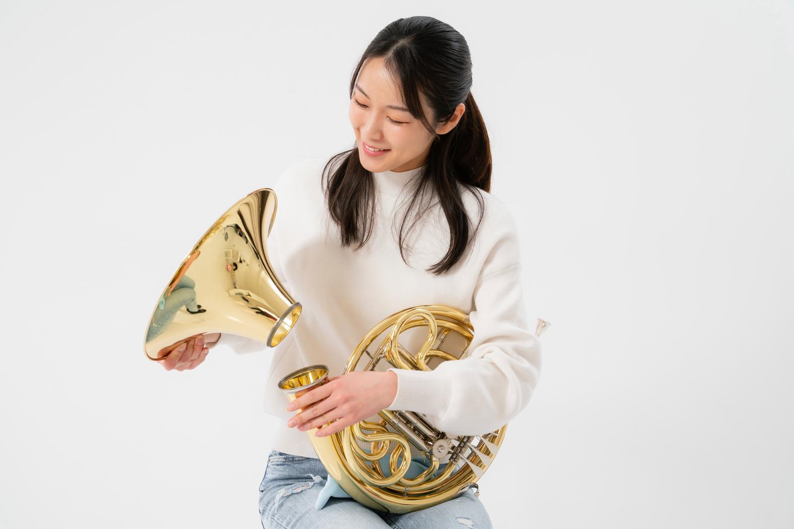 ホルンを持って見つめる白いニット姿の女性［モデル：SAKI］