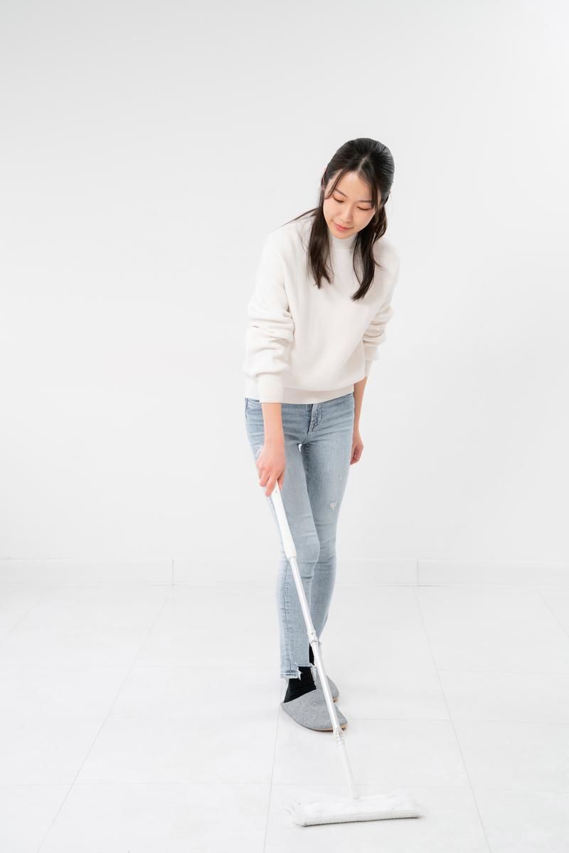白いトレーナーを着た女性が白いモップで床を磨いている［モデル：SAKI］