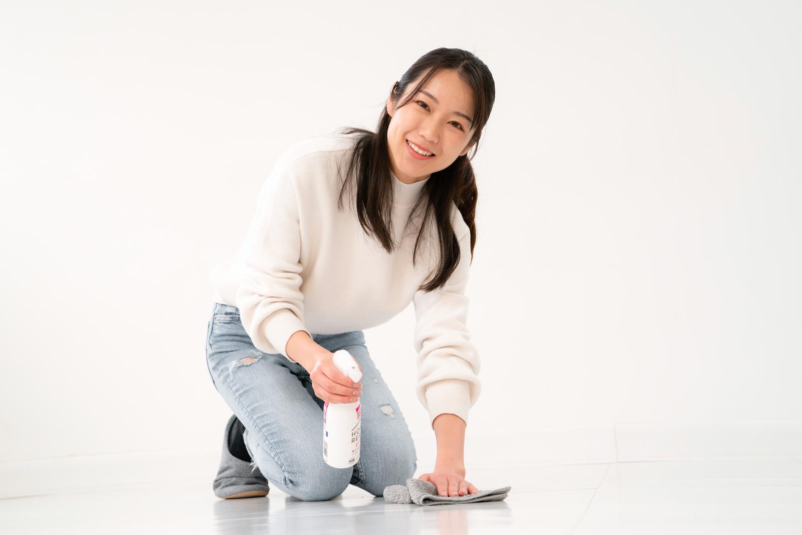 白いニットを着た女性が、スプレーと雑巾で床を掃除している［モデル：SAKI］