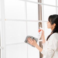 白いスプレー洗剤を使って窓ガラスを拭く女性の写真