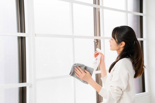 白いスプレー洗剤を使って窓ガラスを拭く女性