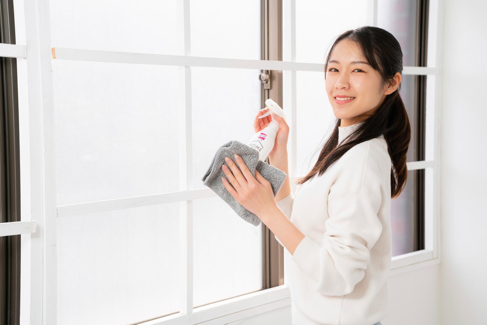 窓ガラスをスプレーとタオルで拭く白いシャツの女性［モデル：SAKI］
