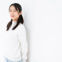 白背景で微笑む女性の自然な表情、長髪と白いトップスのポートレートの写真