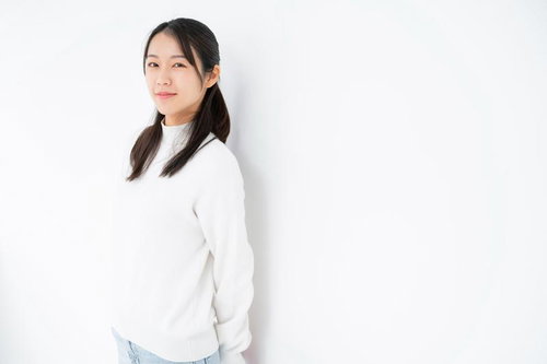 白背景で微笑む女性の自然な表情、長髪と白いトップスのポートレート