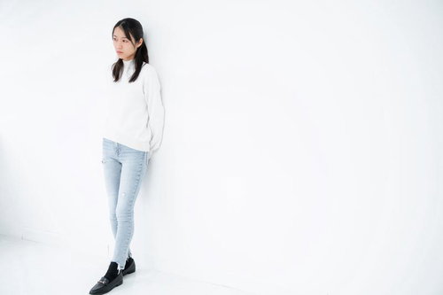 白背景で横向きに立つ不安げな女性のポートレート