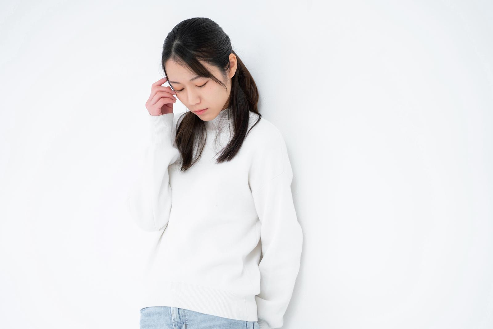白いニットを着た女性が下を向き、手を顔に添えて心配そうな表情をしている［モデル：SAKI］