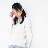 伏し目がちで心配そうな表情の女性、手を顔に添えた悩みのポーズの写真