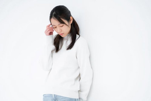 伏し目がちで心配そうな表情の女性、手を顔に添えた悩みのポーズ