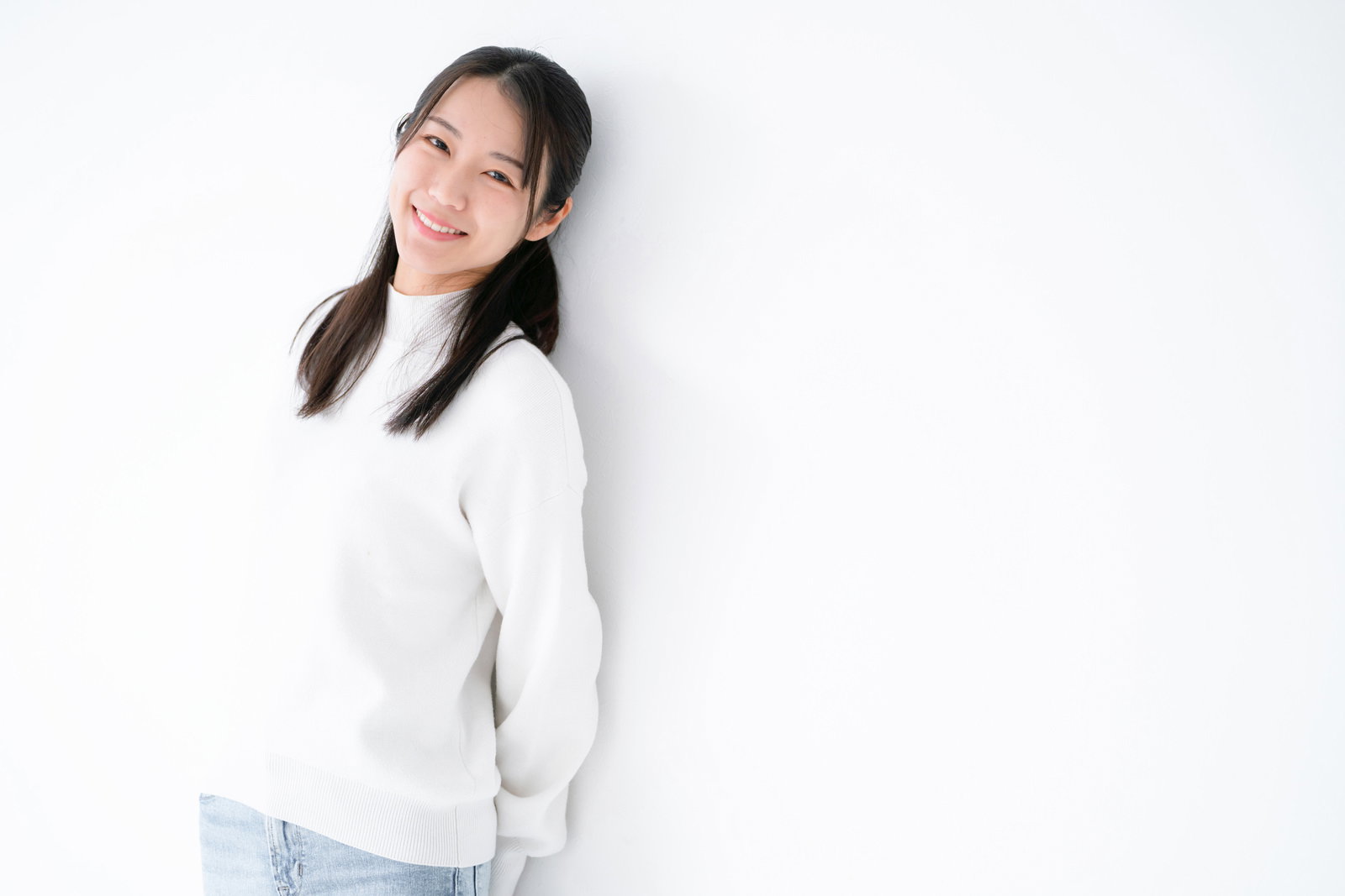 壁に寄りかかりお礼を言う笑顔の女性［モデル：SAKI］