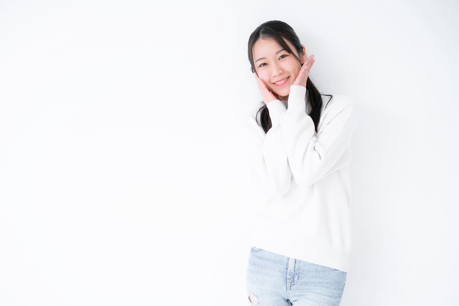 A woman in a white top smiling shyly with her hands on her cheeks