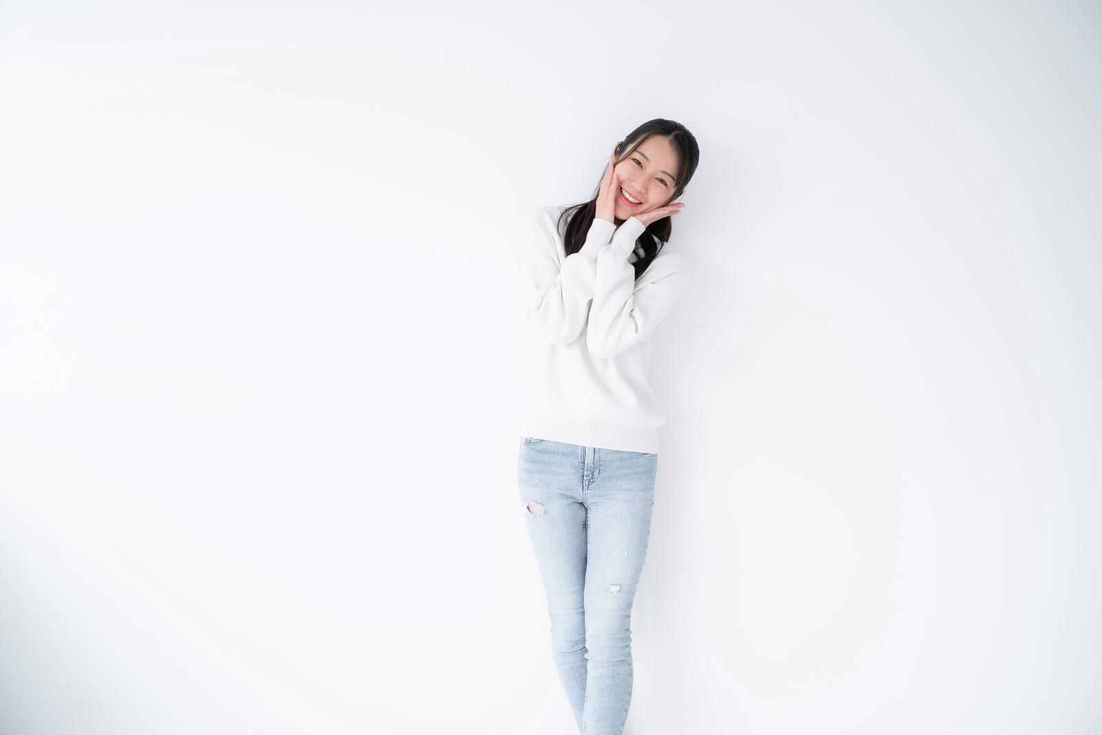 Woman in white sweater shyly smiling with hand on cheek