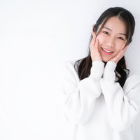 白背景で両手を頬に当てて微笑む幸せを感じる女性の写真