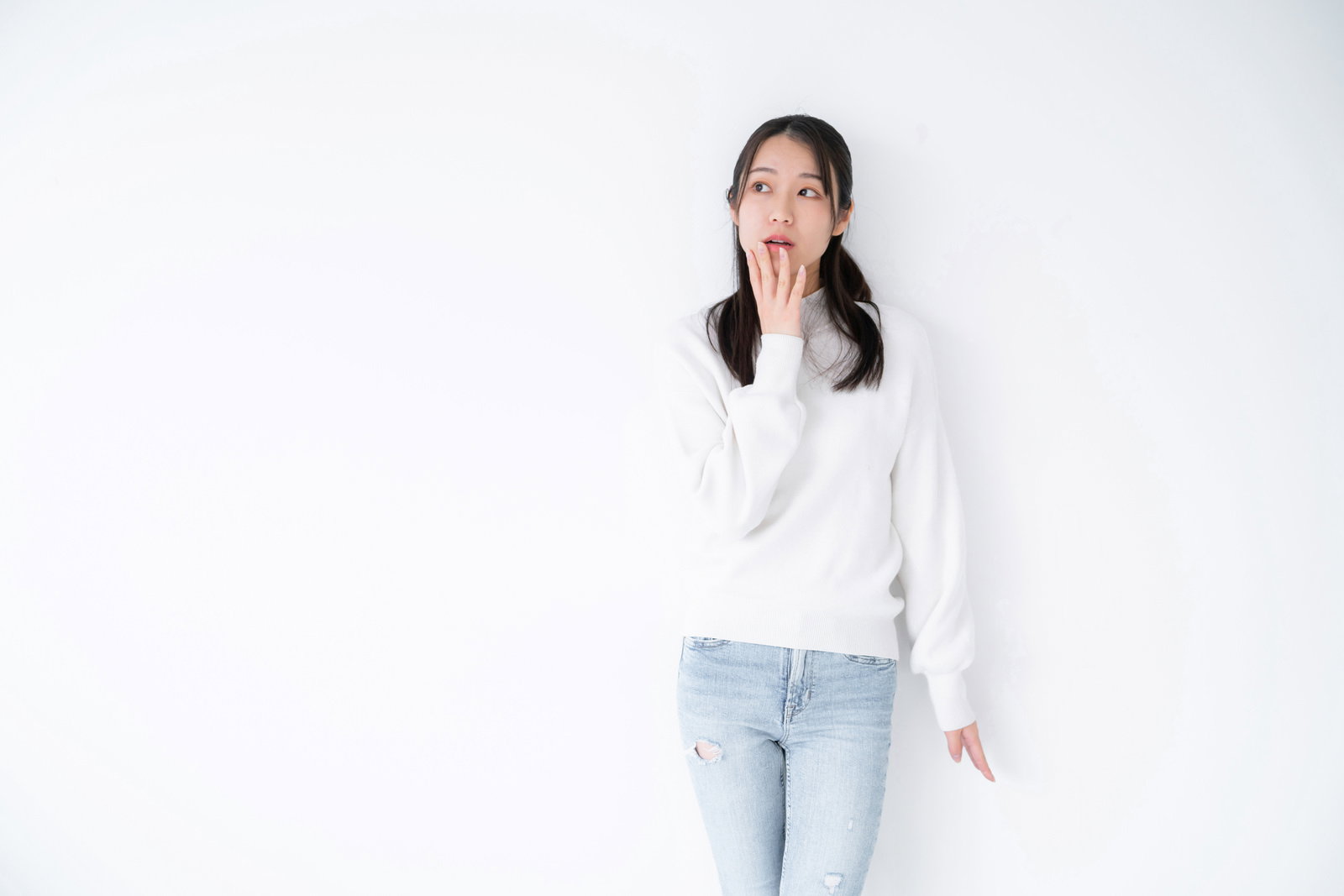 白背景で用事を思い出したような表情を見せる白いニットを着た女性［モデル：SAKI］