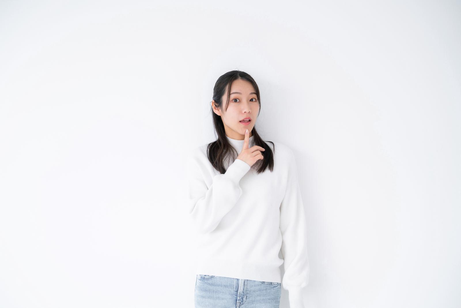 白い長袖を着た女性が驚いた表情で頭の横に手を当てている［モデル：SAKI］