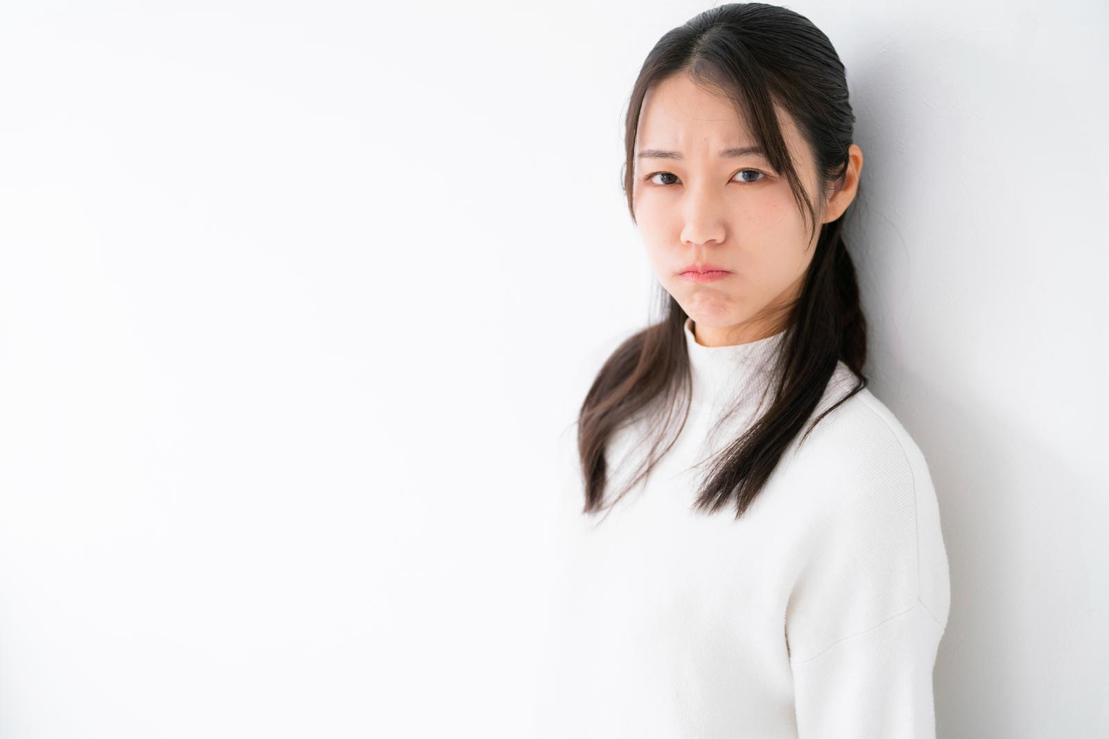 A woman in a white turtleneck leaning against a wall with a sullen expression