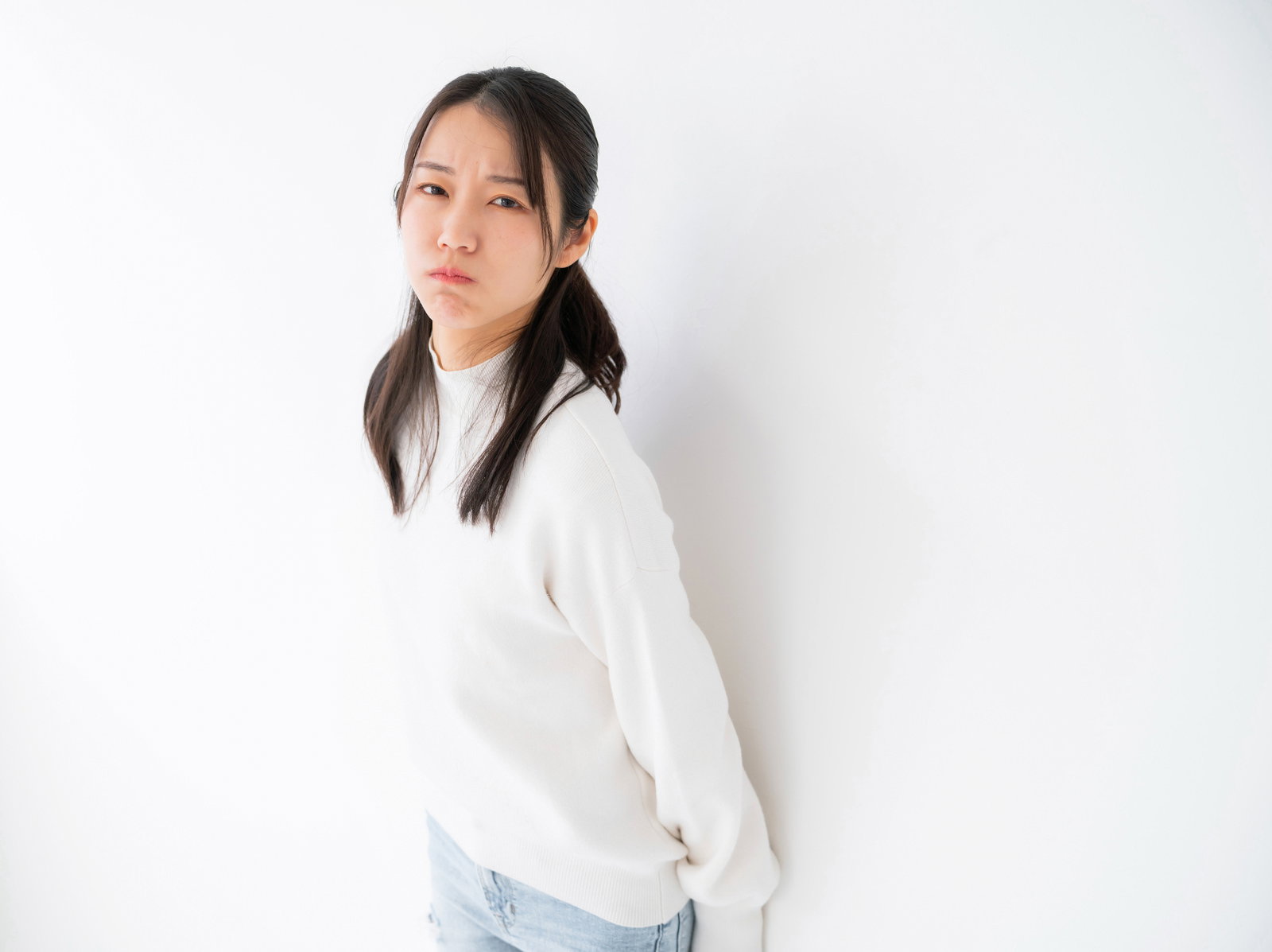 白いトップスを着た女性が不機嫌そうな表情をしている［モデル：SAKI］