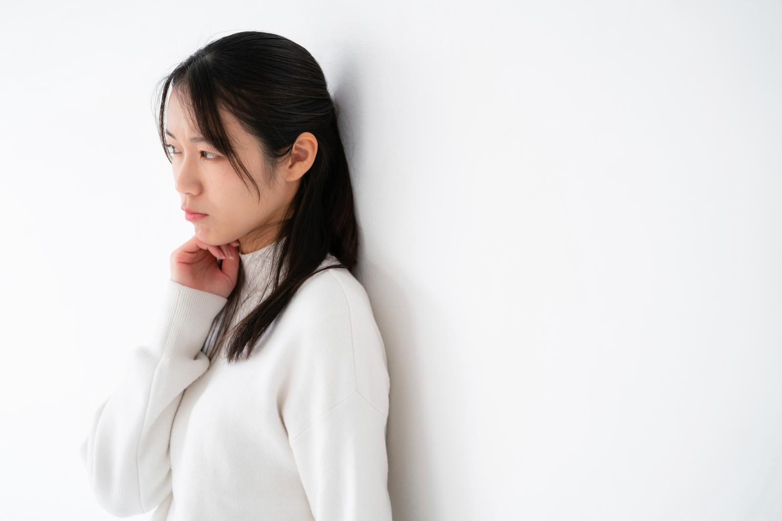 A woman in a white turtleneck standing with her head resting on her hand and her gaze averted