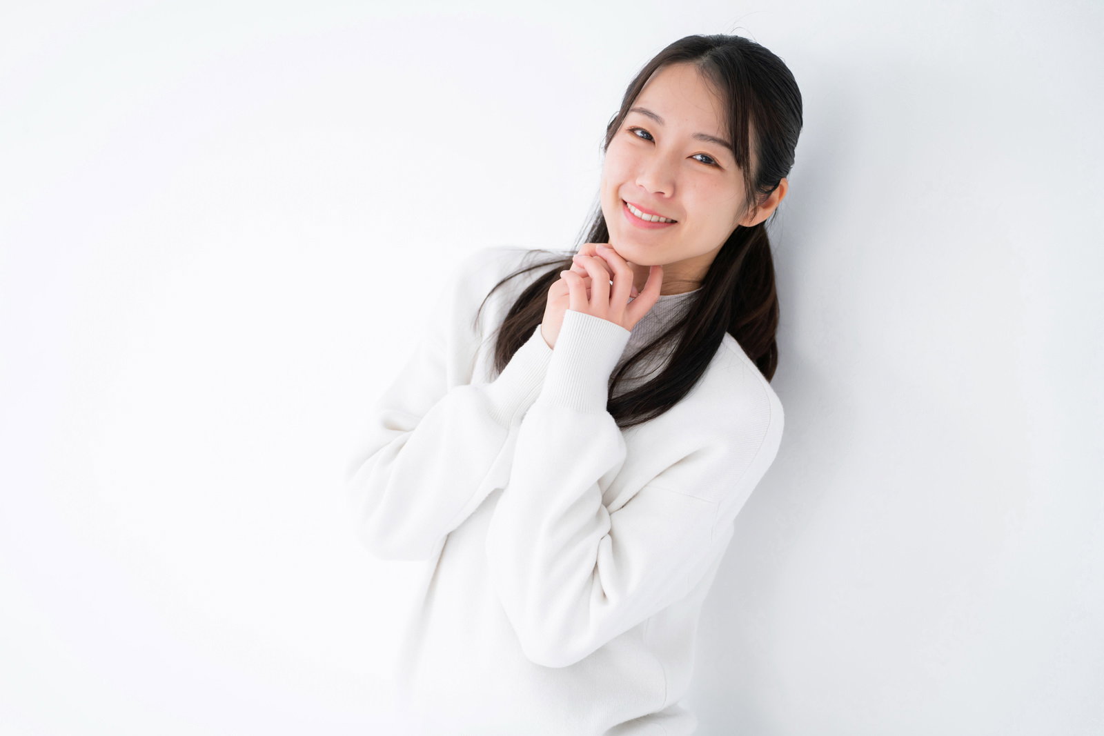 白背景で手を合わせておねだりするポーズをとる笑顔の女性［モデル：SAKI］