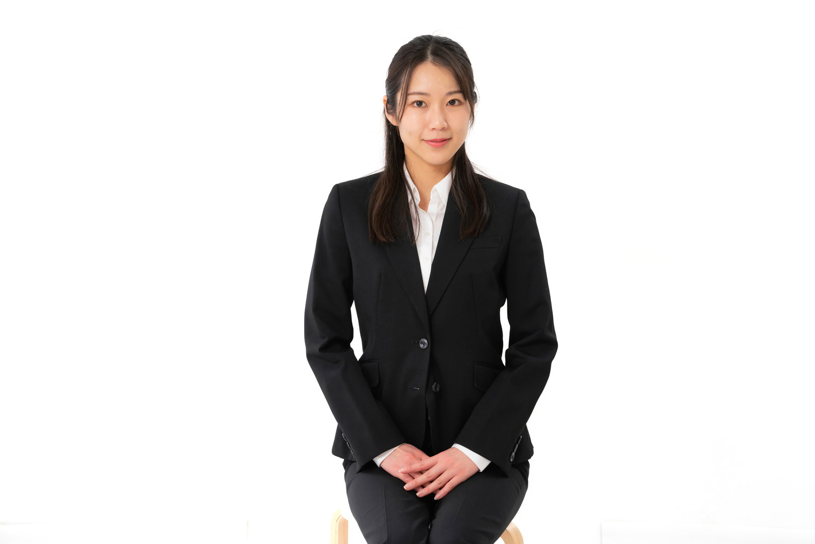 黒いスーツを着用し手を組んで立つ女性社員［モデル：SAKI］