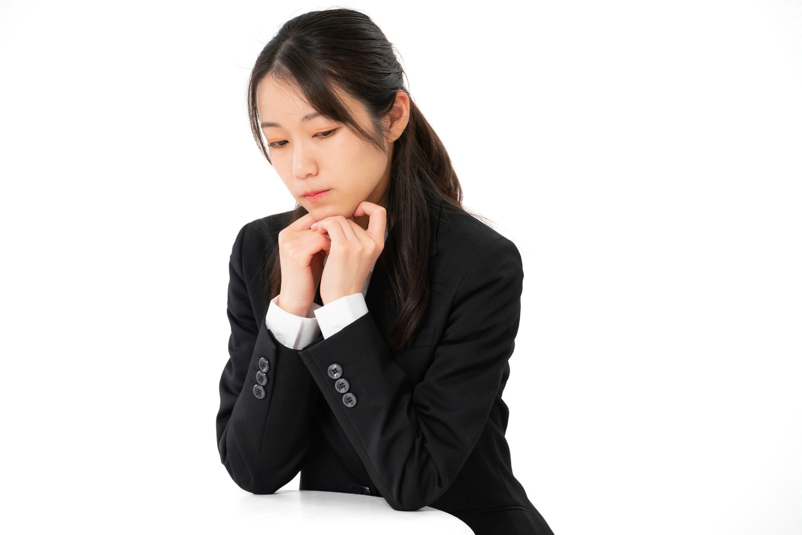 黒いスーツを着た女性が手を顔に当てて悩んでいる様子［モデル：SAKI］