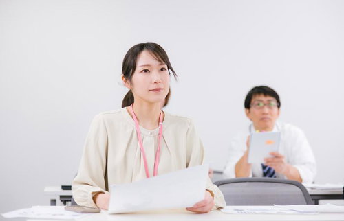 白い会議室で資料を持ち真剣にミーティングに参加する女性社員