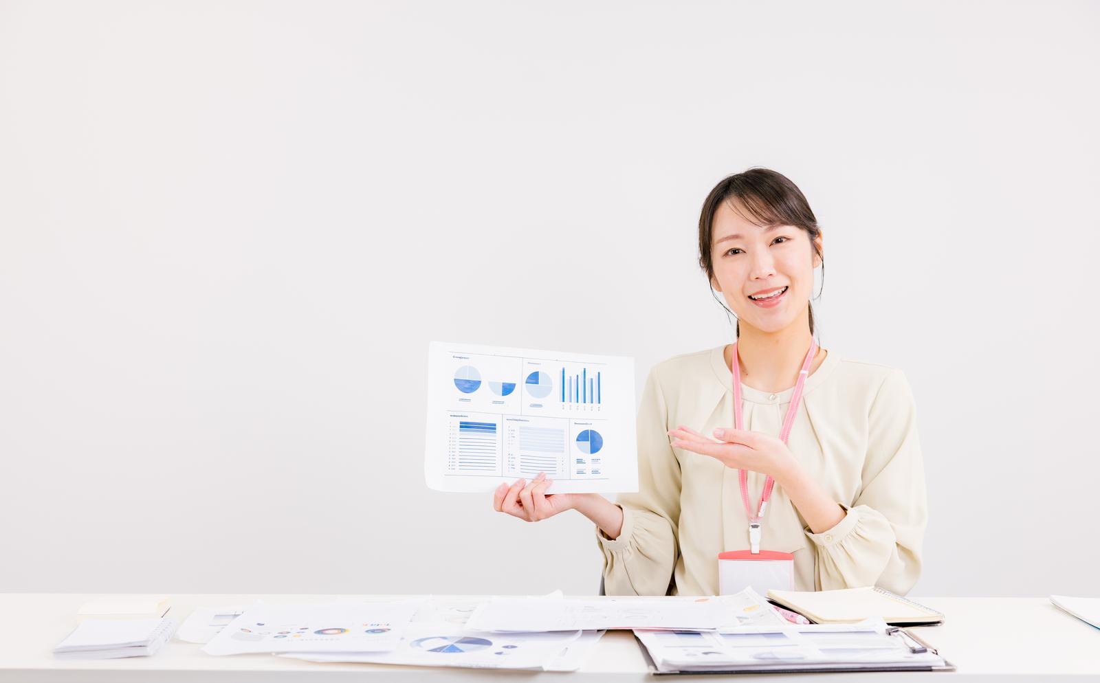 データ分析レポートを手に説明するビジネスカジュアル姿の女性［モデル：SAKI］