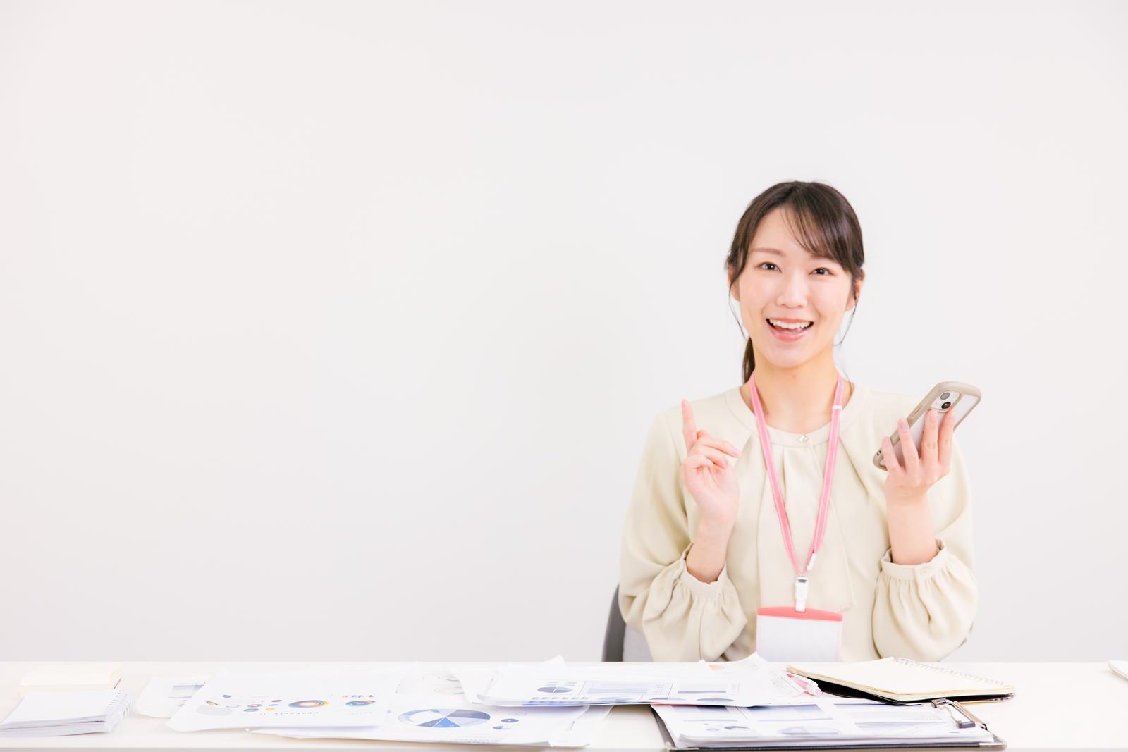 スマートフォンを持ちながら資料を案内する笑顔の女性マネージャー［モデル：SAKI］