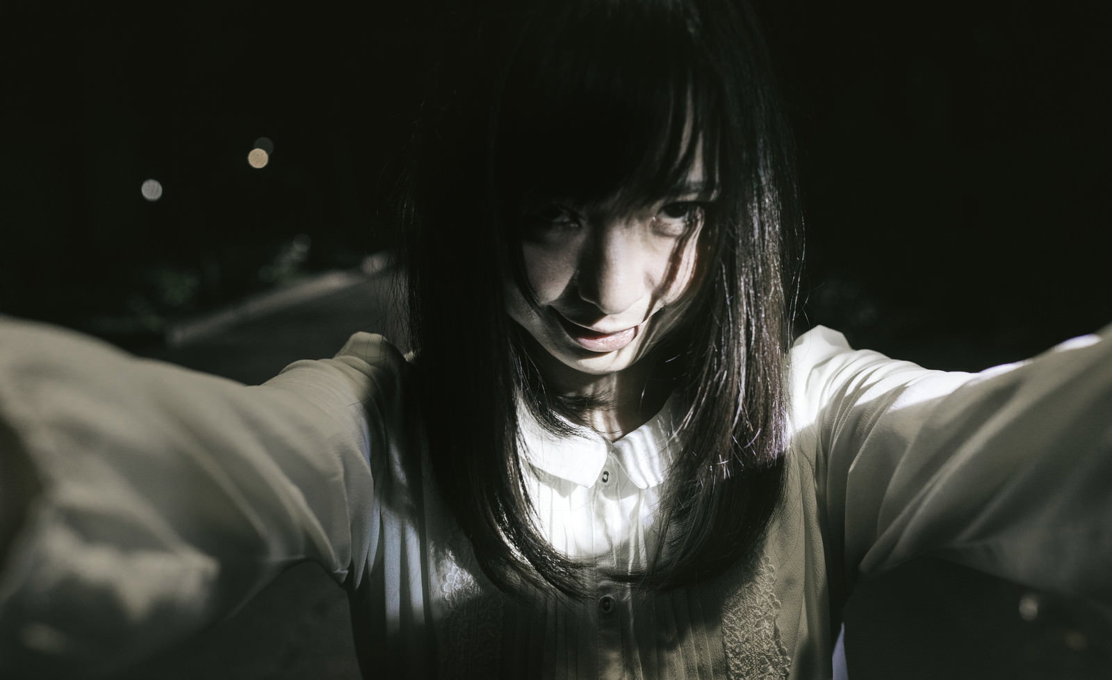 暗闇の中で両手を広げる長い髪の女性、豹変した表情でホラーな雰囲気［モデル：さとうゆい］