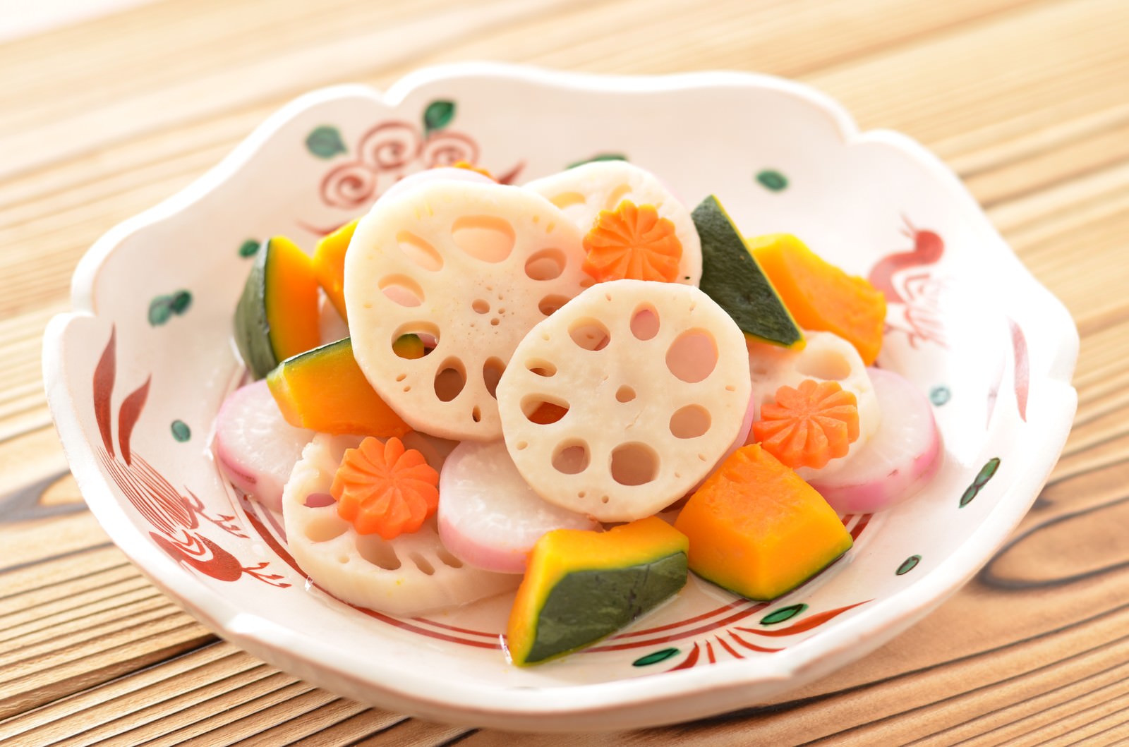 白い器に盛り付けたれんこんと野菜の煮物。穴の開いたれんこん、にんじン、竹の子が組み合わさっている