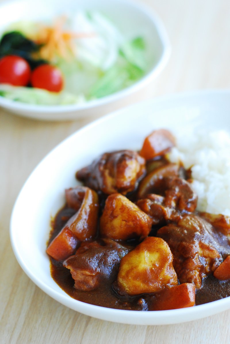 白い皿に盛られたカレーとご飯、背景にサラダの定食