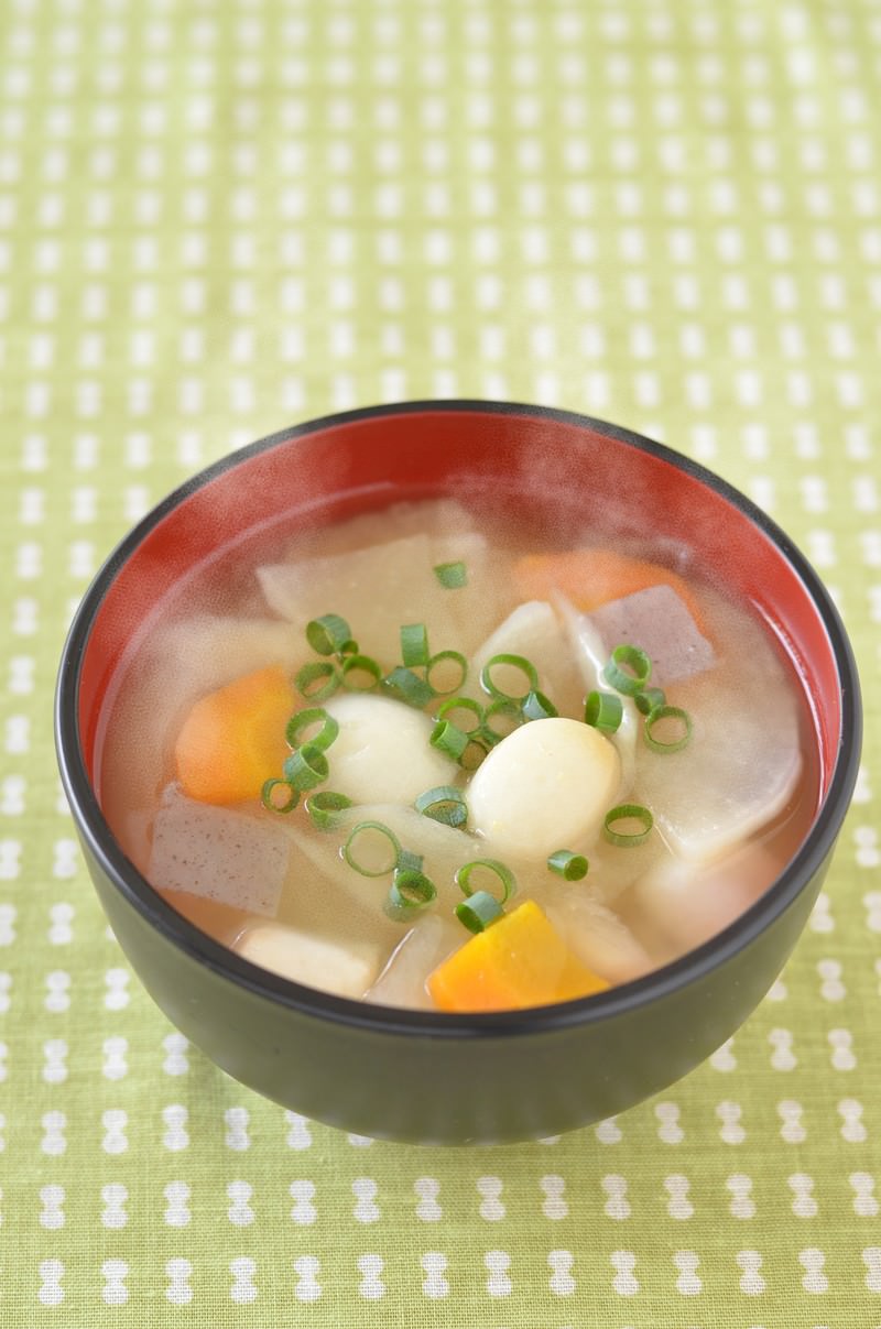 赤い椀の豚汁に里芋、豆腐、人参、豚肉が入り青ねぎが散らされている