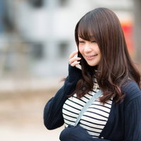 スマホの電話ごしに伝わる笑顔、ボーダーシャツの長髪女性の写真