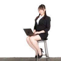 ハイスツールに座ってノートパソコンを操作するビジネス女性の写真