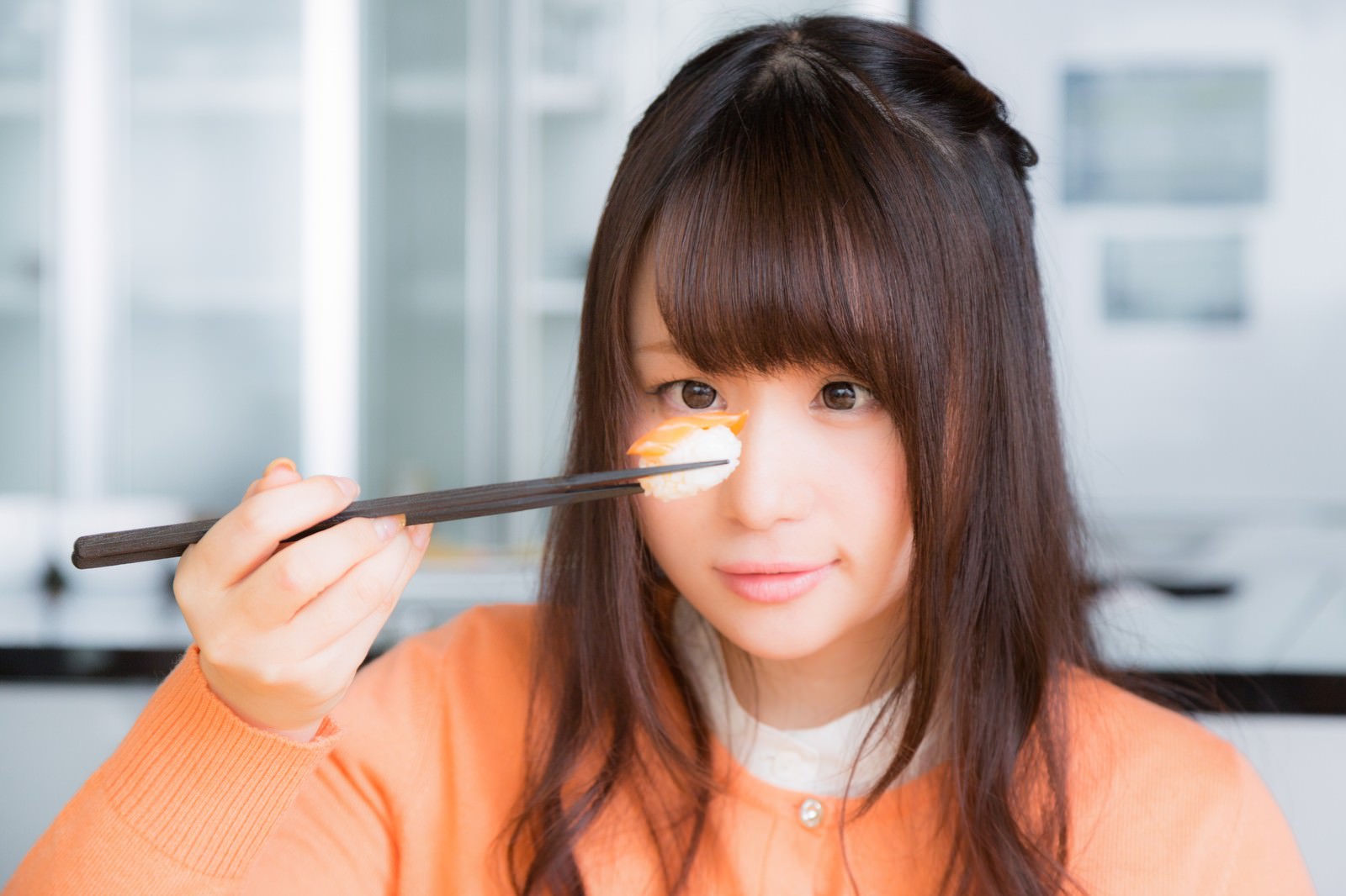 寿司を前に葛藤する表情の女性が箸で握り寿司を持っている［モデル：茜さや］