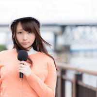 災害現場からニュースを伝えるヘルメット着用の女性アナウンサーの写真