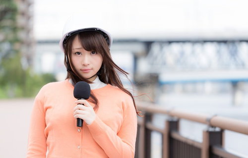 災害現場からニュースを伝えるヘルメット着用の女性アナウンサー