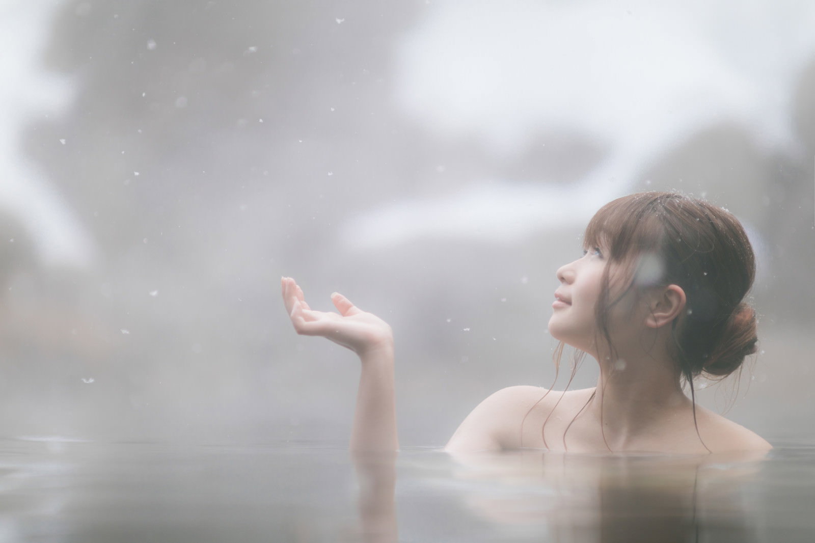雪が降る中、露天風呂で入浴しながら手を差し出す女性の後ろ姿［モデル：茜さや］