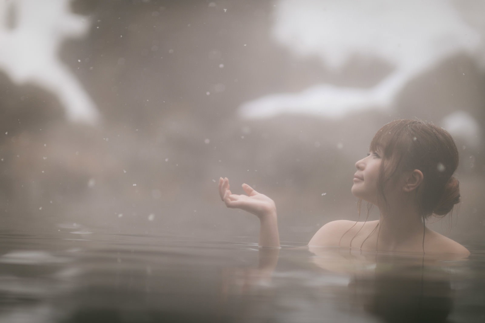 粉雪舞う露天風呂で雪を眺めながら入浴している女性の後ろ姿［モデル：茜さや］